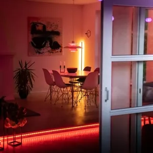 Lite Bulb Moments RGB-LED-listbelysning under en upphöjd golvkant i en matsal med varmt rosa-rött stämningsljus.