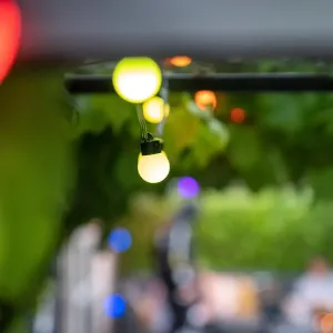 Lite Bulb Moments smart ljusslinga med lysande klotlampor i flera färger, upphängd i en utomhusmiljö