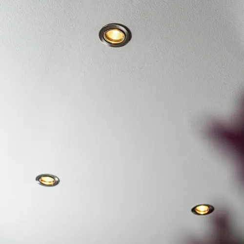 GU10 LED-lambi sisseehitatud ümmargune metallist rõngaga laevalgusti särab soojalt; kaks samasugust valgustit paistavad kaugemal valges laes.