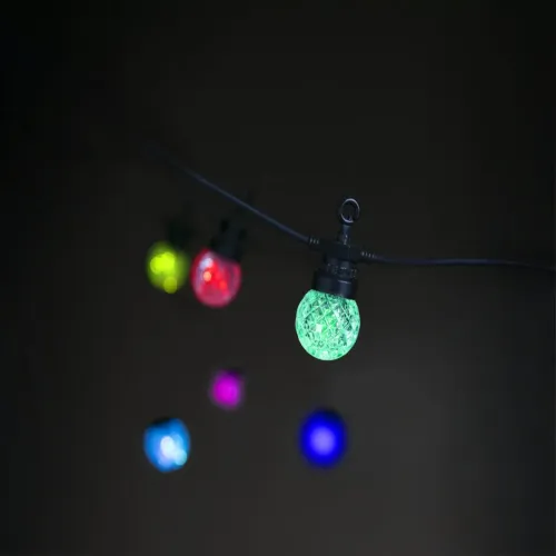 Lyskæde med facetterede globelys på sort kabel, flerfarvede glødende kugler med grønt lys i fokus mod mørk baggrund.