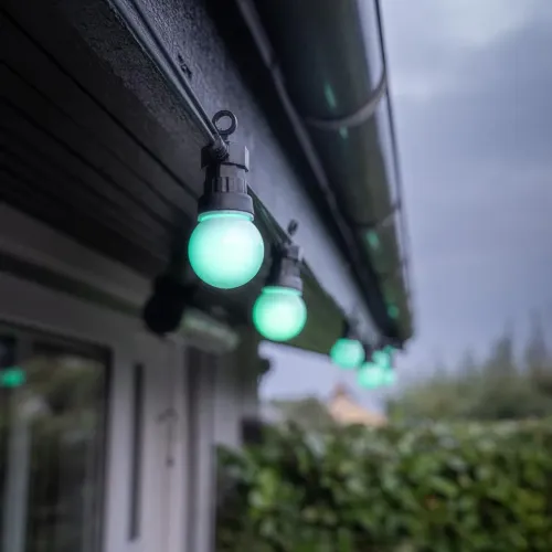 Gaismas ķēde ar apaļām spuldzītēm melnos turētājos, kas uzstādītas gar karnīzi ārā, zaļas gaismas lodītes vienmērīgi izvietotas.