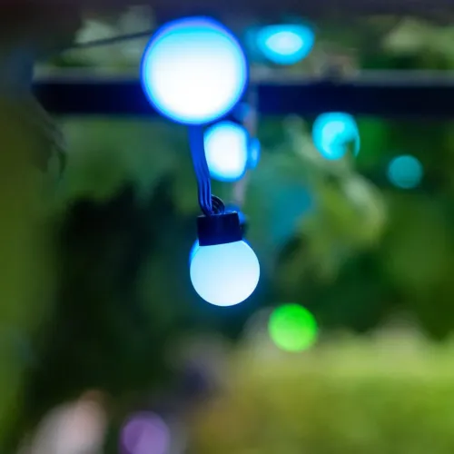 Smart lyskæde med små kugleformede lys, der lyser blåt, udendørs på kabel med sort fod, sløret bokeh i baggrunden.