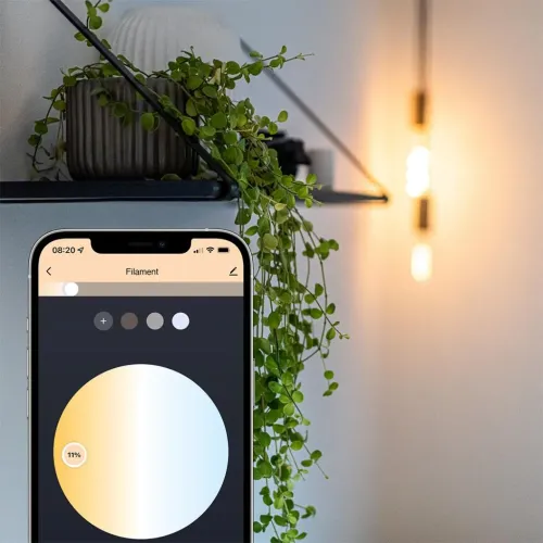 E27-pæren lyser varmt i baggrunden, mens smartphonen viser appens farveslider i forgrunden af mobilskærmen.